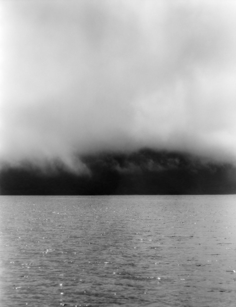 Low cloud drifting over a dark treeline and still water